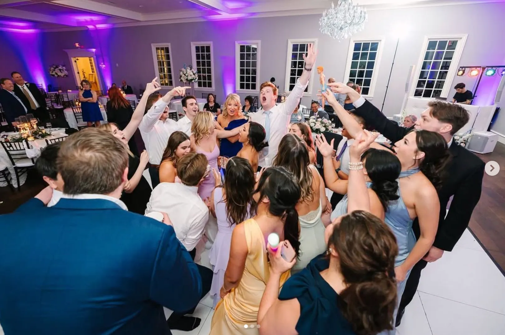 A packed dance floor under purple uplights at a wedding reception
